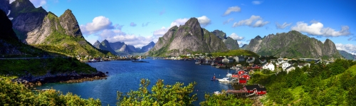 Reine in Lofoten Islands, Norway, with traditional red rorbu huts under blue sky with clouds. 