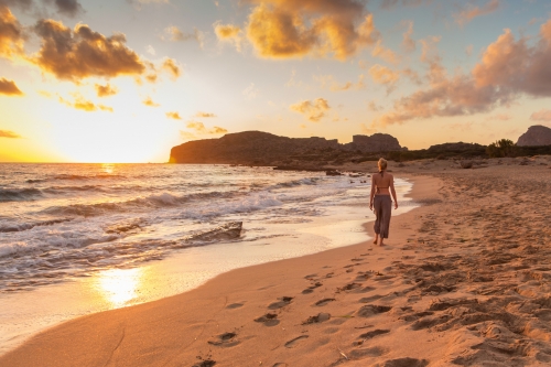 Woman walking on sandy beach at golden hour. Seashore sunset walk, Falasarna, Crete, Greece.