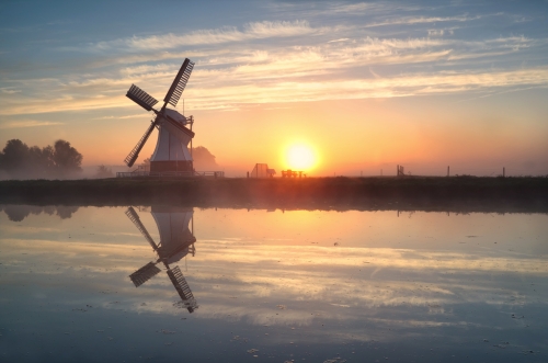 Dutch windmill reflected in river at sunrise