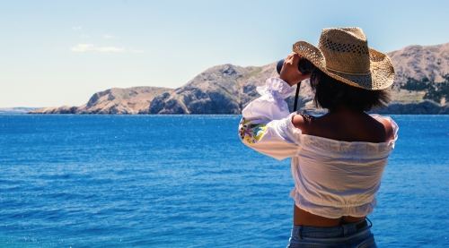 Frau schaut mit Fernglas aufs adriatische Meer
