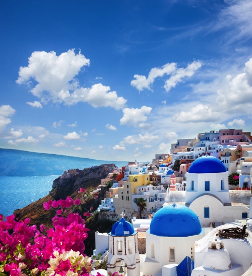 Oia, traditional greek village of Santorini with blue domes of churches under sky with flowers, Greece