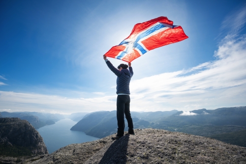Frau mit einer wehenden norwegischen Flagge vor einem Naturhintergrund.