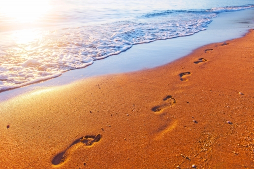 Strand, Wellen und Fußabdrücke bei Sonnenuntergang