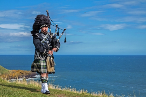 Traditionelle schottische Dudelsackspieler in voller Dresscode mit dem Meer im Hintergrund