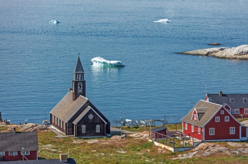 Alte hölzerne Zions-Kirche in Ilulissat (Disco-Bucht mit Eisbergen auf Hintergrund), Westgrönland