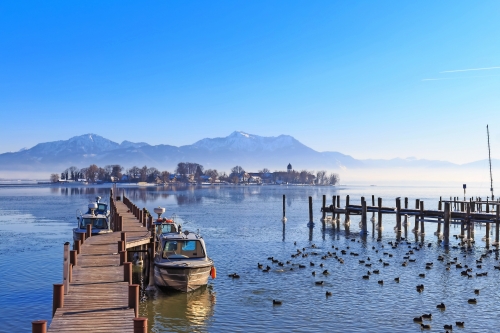 Boote an der Anlegestelle in Gstadt, Bayern, Deutschland, mit See Fraueninsel im Hintergrund an einem kalten Wintertag